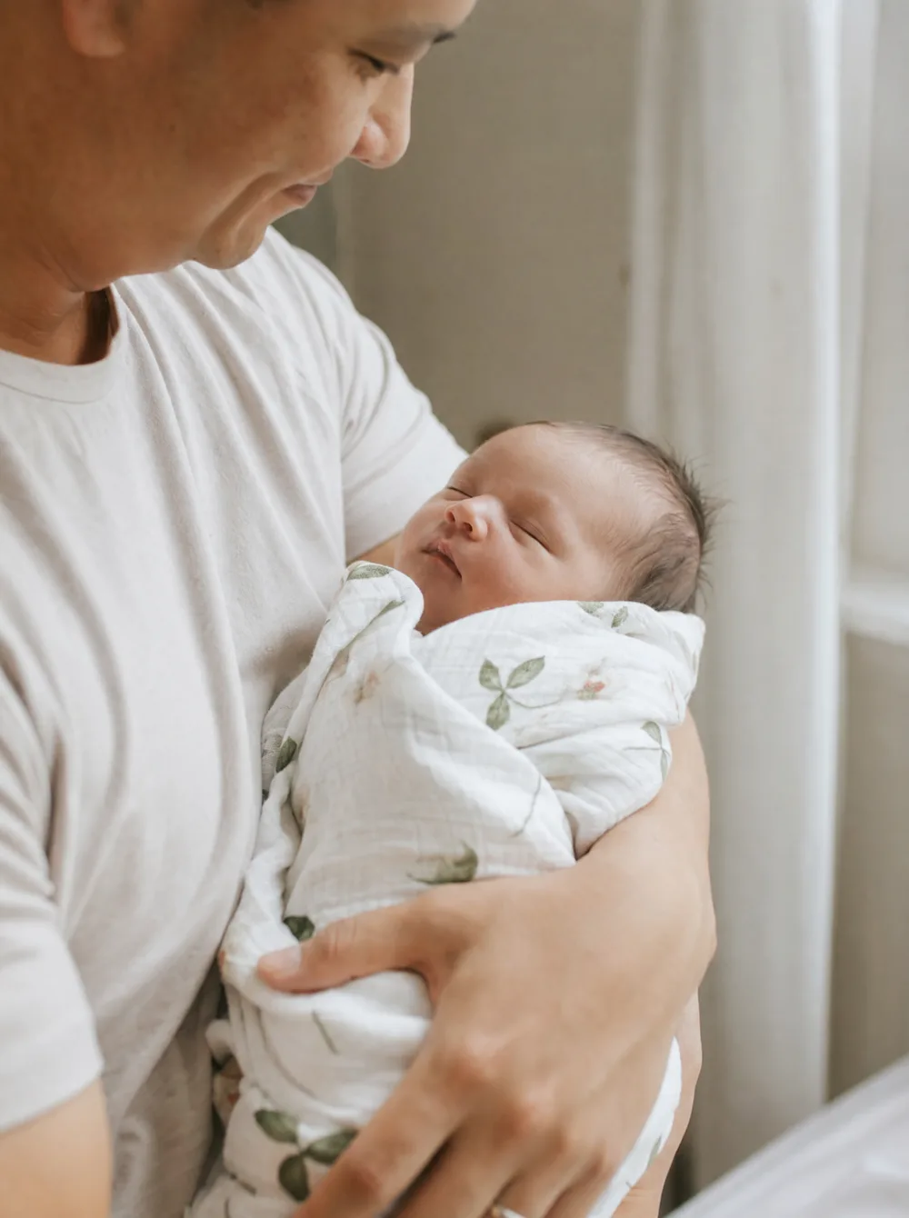 Newborn cradled gently in a parent's arms, soft natural light, muted neutral tones