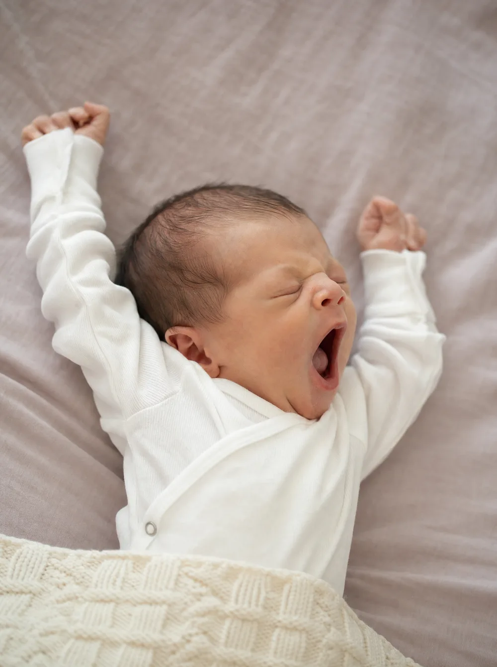 Newborn baby yawning and stretching, soft natural light, gentle detail shot